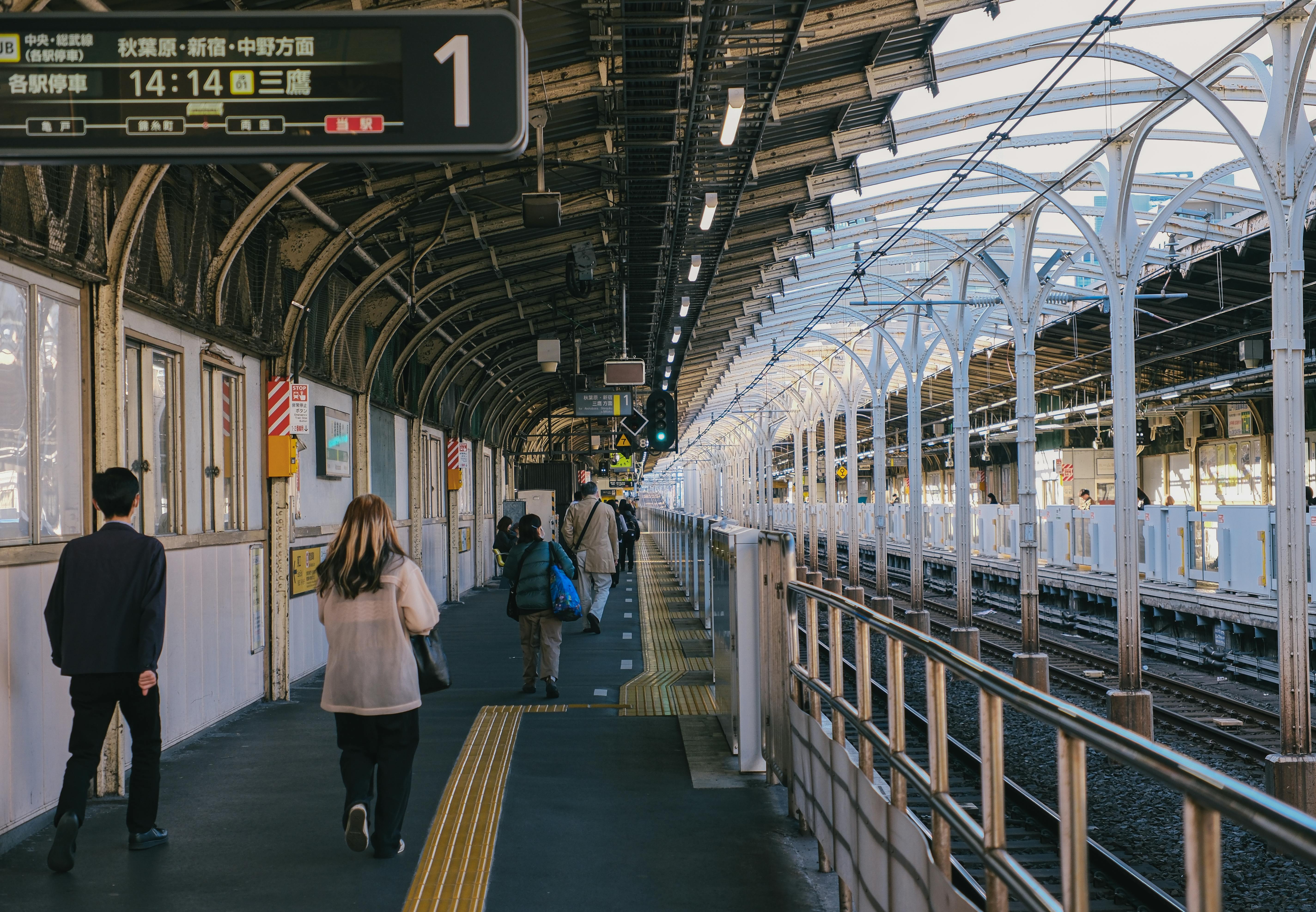 Commuters walking along a bustling train station platform under a covered structure.