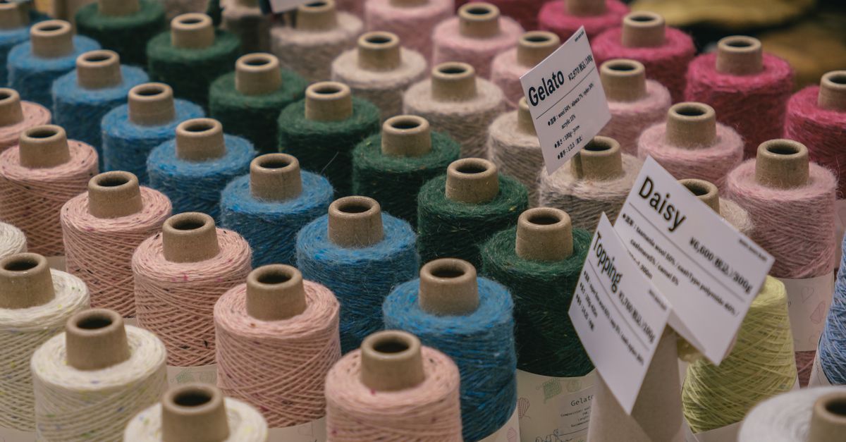 A variety of colorful yarn spools on display at a craft market, labeled with unique names.