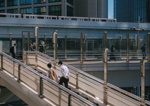 Free Cityscape scene of people commuting on a pedestrian bridge with train in background. Stock Photo