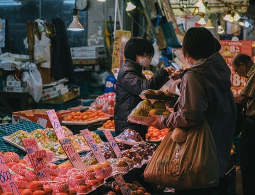 Free Vibrant market scene with shoppers exploring diverse fresh fruits under warm lighting. Stock Photo