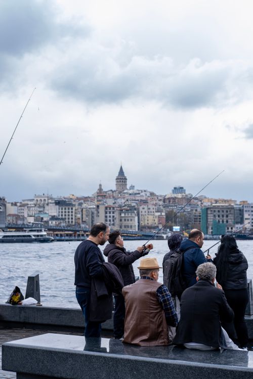 Free A group of men fishing on Galata Bridge with Istanbul's cityscape in the background on a cloudy day. Stock Photo