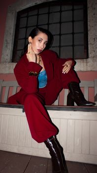 Fashion-forward woman in red suit posing confidently indoors with modern accessories.