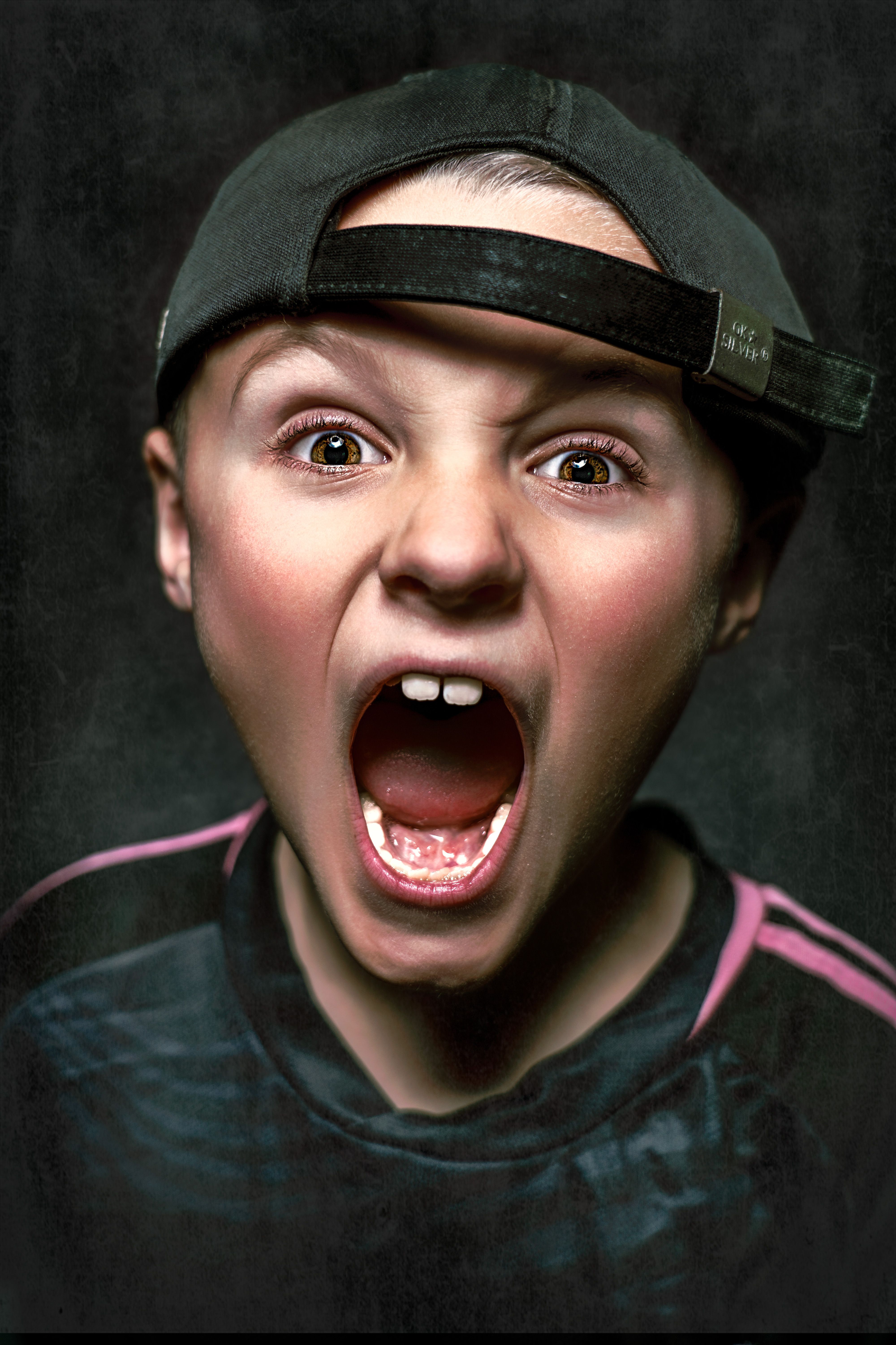 Portrait of a young boy shouting with excitement, wearing a backwards cap in Manchester, UK.