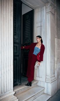 Woman in red suit standing at classical door, striking a fashion pose.