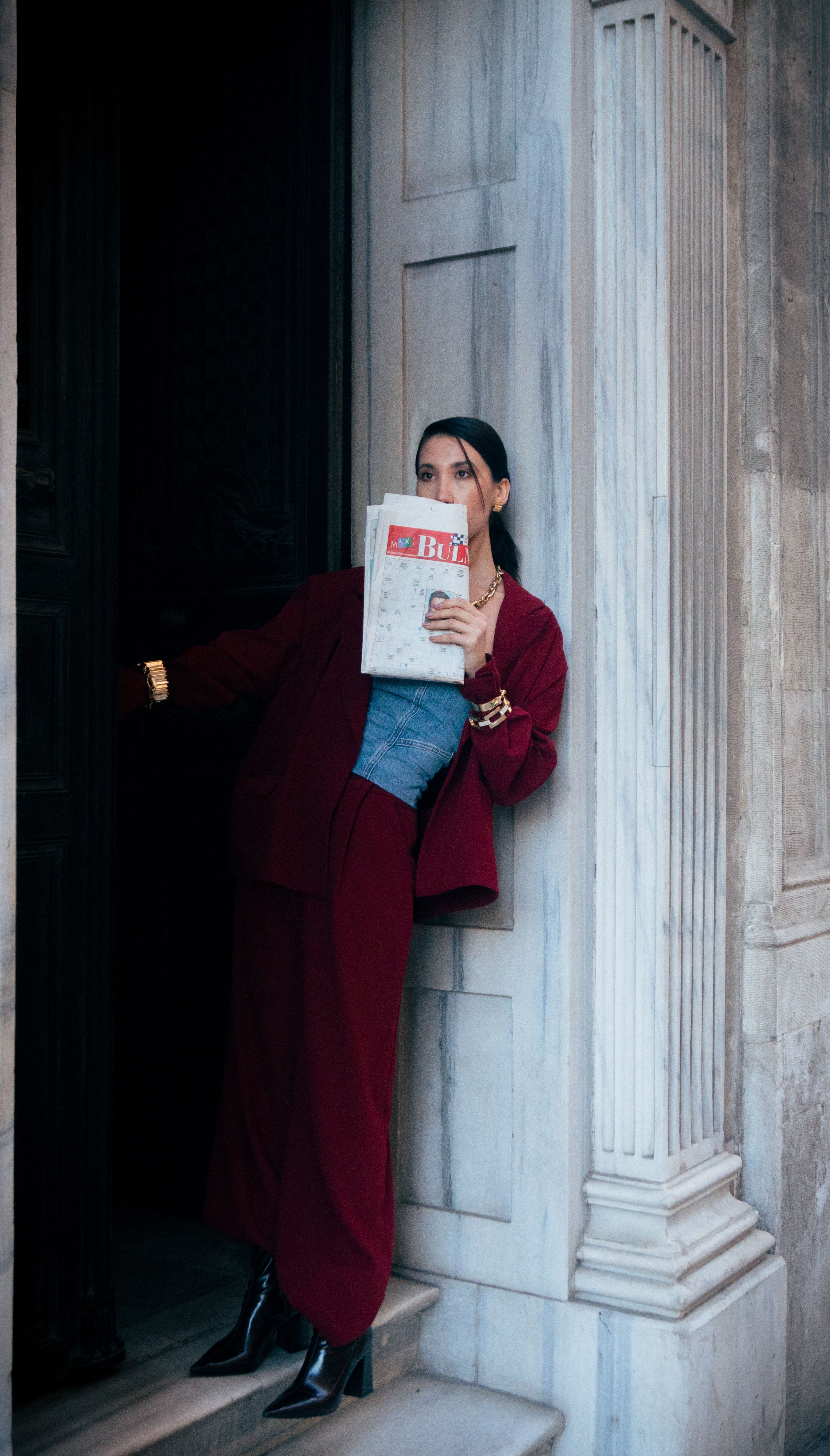 Fashionable woman in red suit with newspaper at marble entrance.