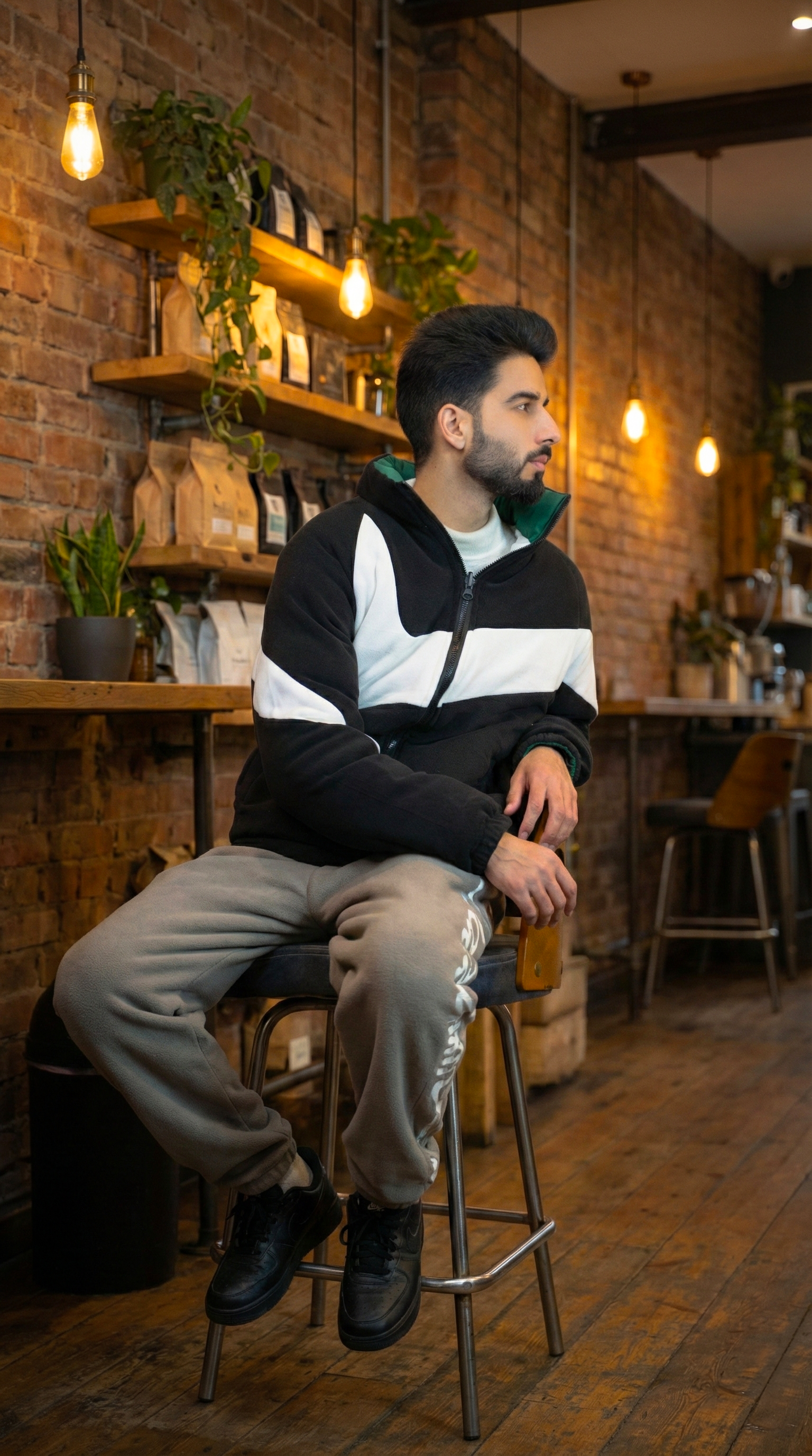 A fashionable man sits in a stylish coffee shop with warm lighting and rustic decor.