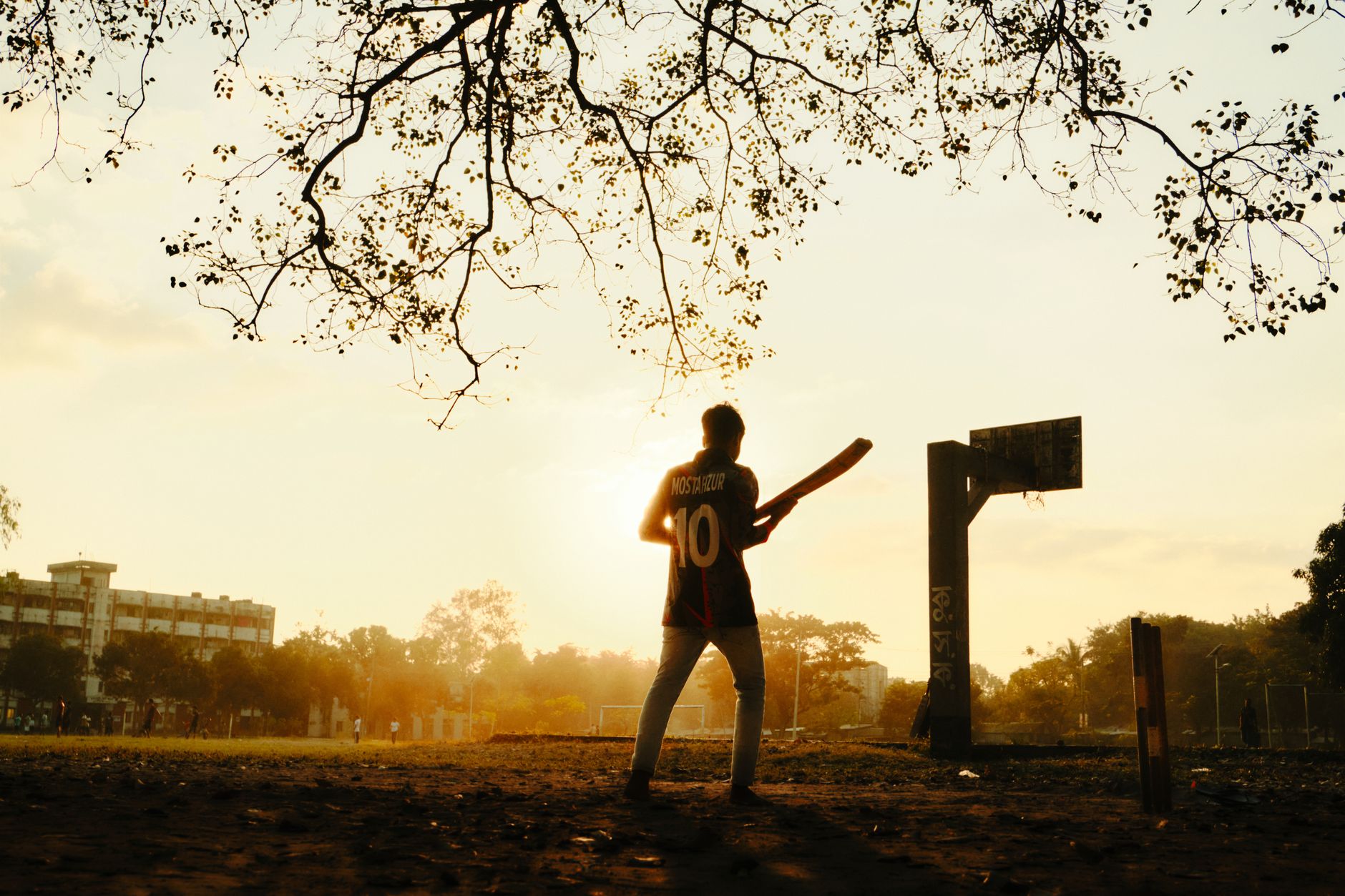 A boy plays cricket in a field during sunset in Kurigram, Bangladesh.