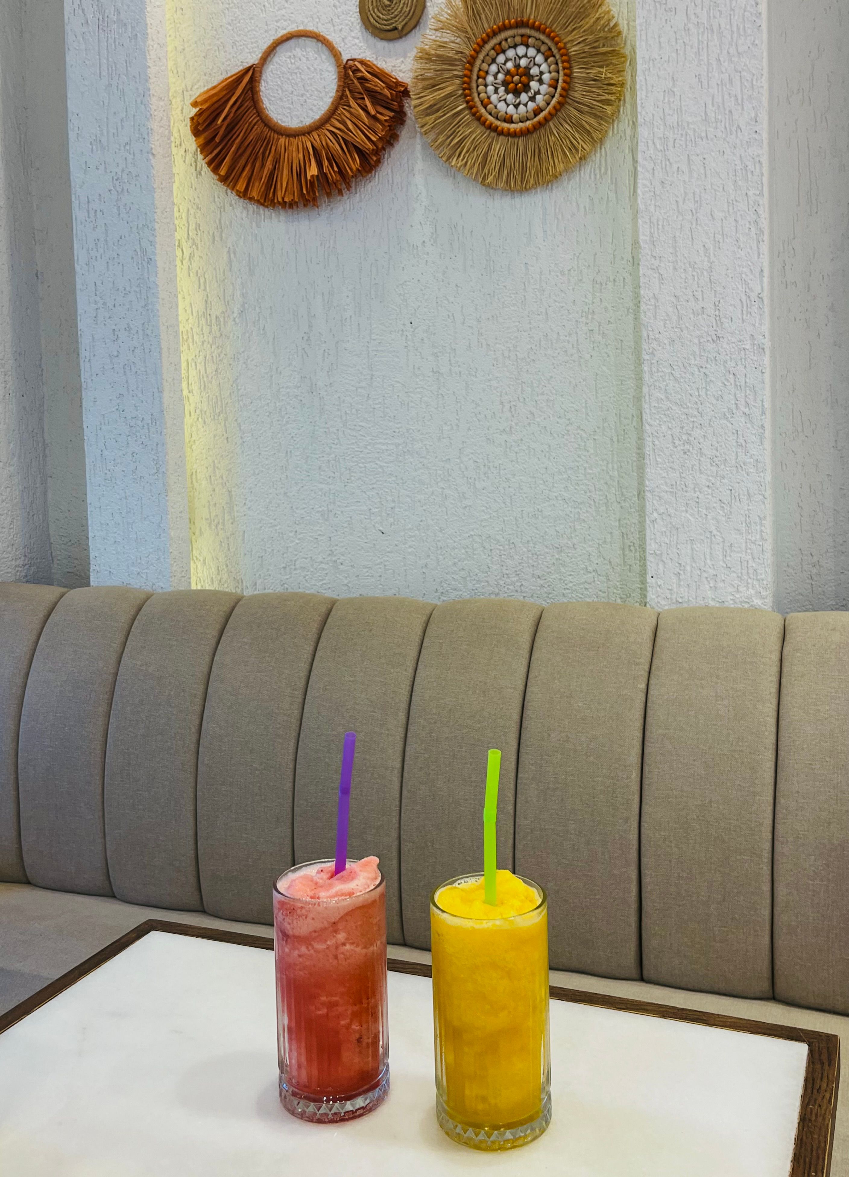Two vibrant fruit smoothies on a minimalist cafe table surrounded by stylish boho decor.