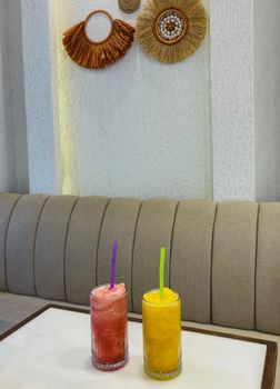 Two vibrant fruit smoothies on a minimalist cafe table surrounded by stylish boho decor.