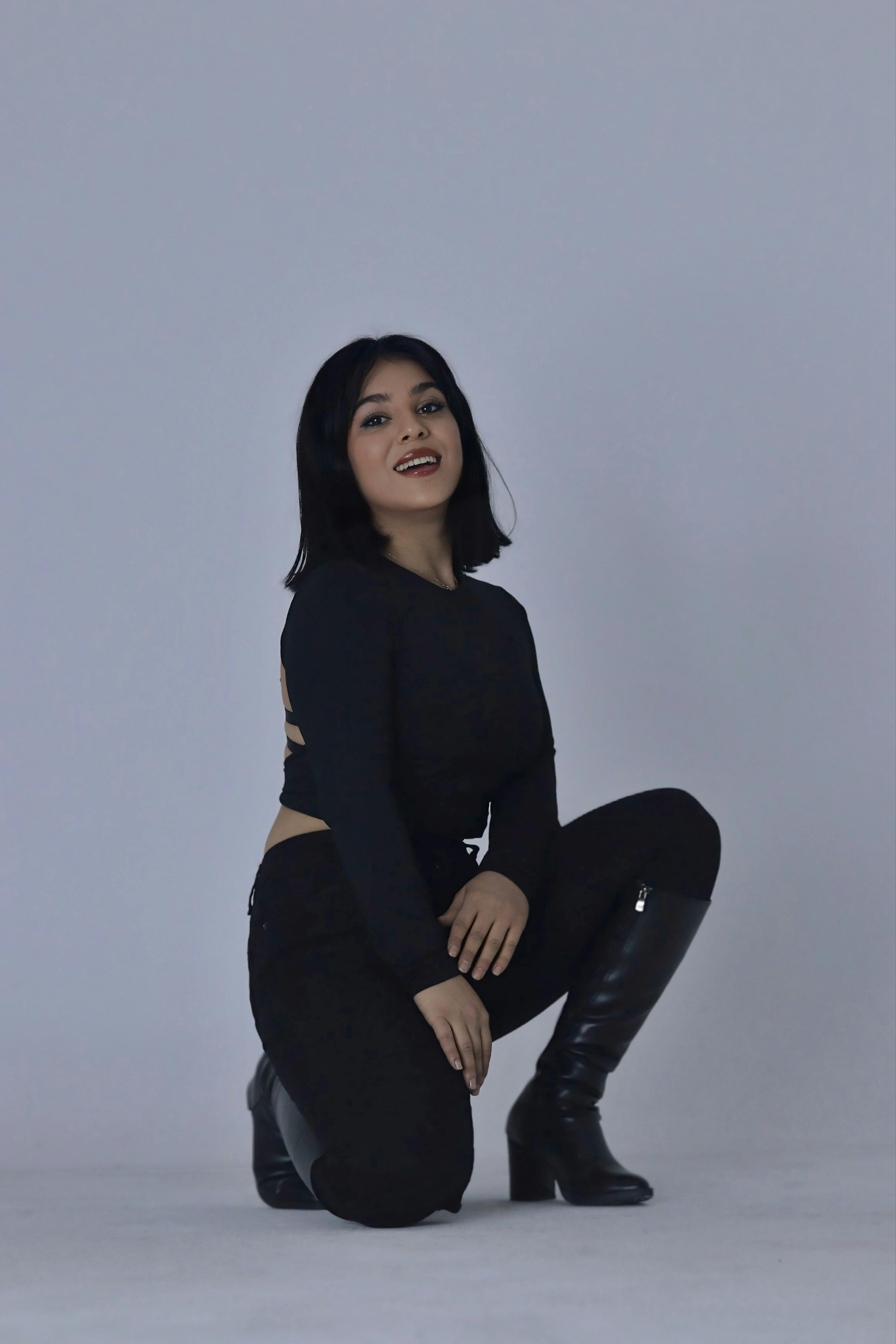 A fashionable young woman poses confidently in a sleek black outfit with boots.