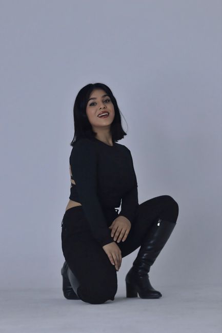 A fashionable young woman poses confidently in a sleek black outfit with boots.