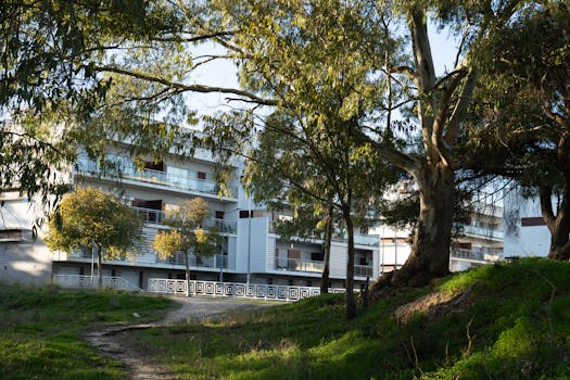 A contemporary residential building in Portugal framed by flourishing trees under a clear sky.