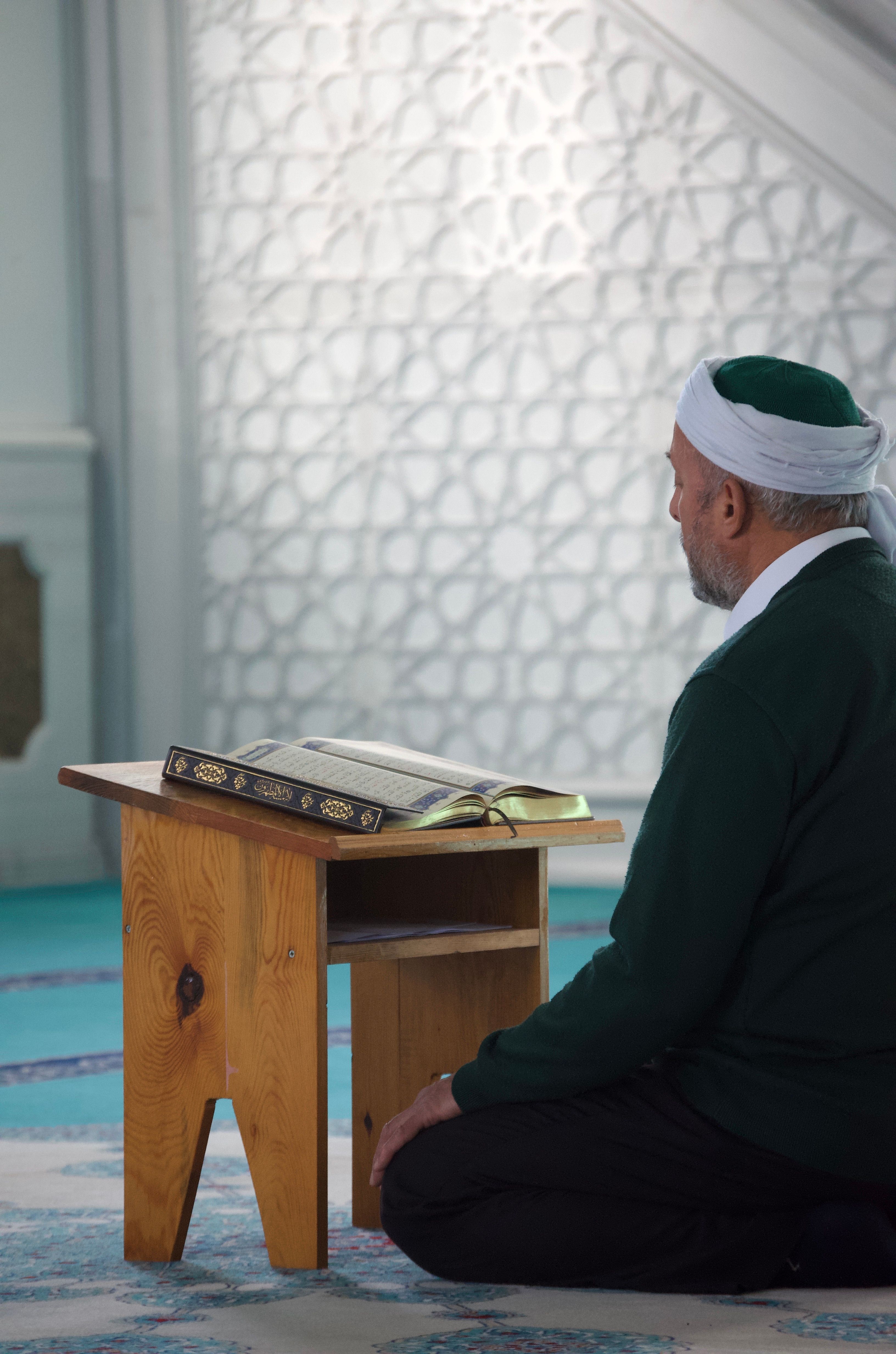 An elderly man deeply engaged in prayer beside an open Quran in a mosque in Türkiye.