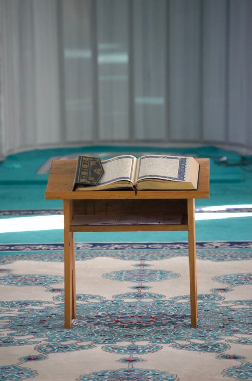 Free An open Quran rests on a wooden stand in a mosque, highlighting Islamic culture and spirituality. Stock Photo
