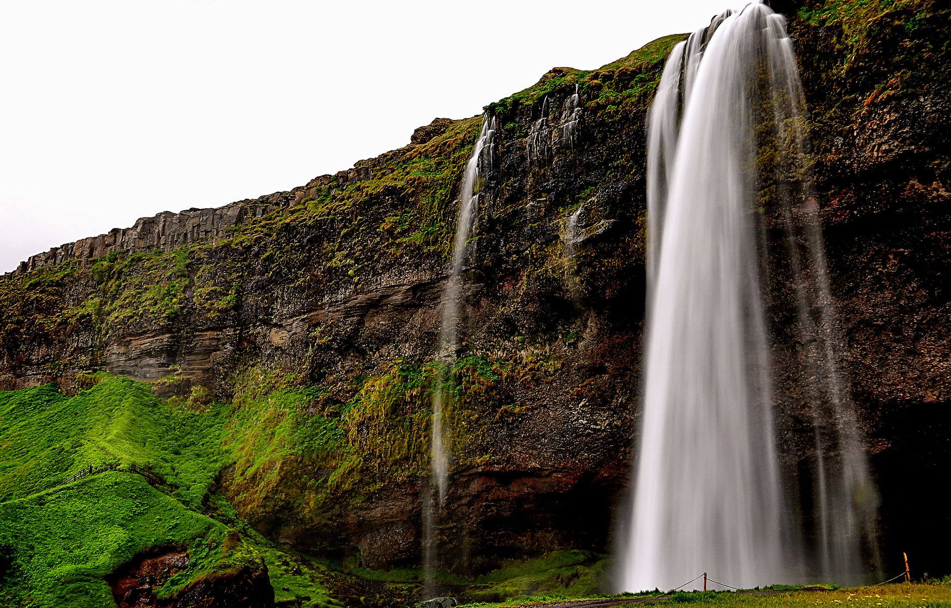 Looking up at a waterfall cascading through a narrow rock opening into a dark cavern