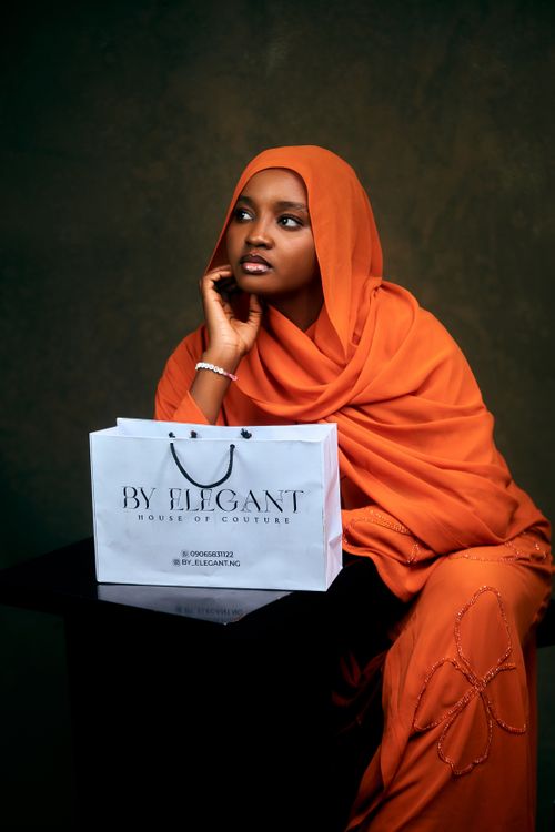 Free Woman in orange hijab posing with a By Elegant shopping bag, exuding grace and poise. Stock Photo