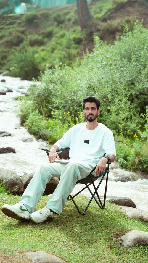 Free A man sits in a chair by a river in the lush, green landscape of Kashmir, surrounded by nature. Stock Photo