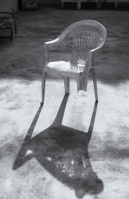 Free Artistic black and white photo of a plastic chair casting a shadow on a concrete floor. Stock Photo