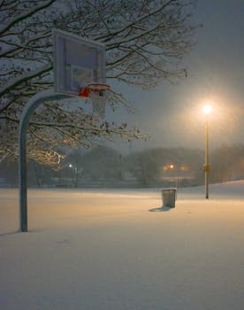 Quiet snowy basketball court illuminated by a streetlight on a winter night.