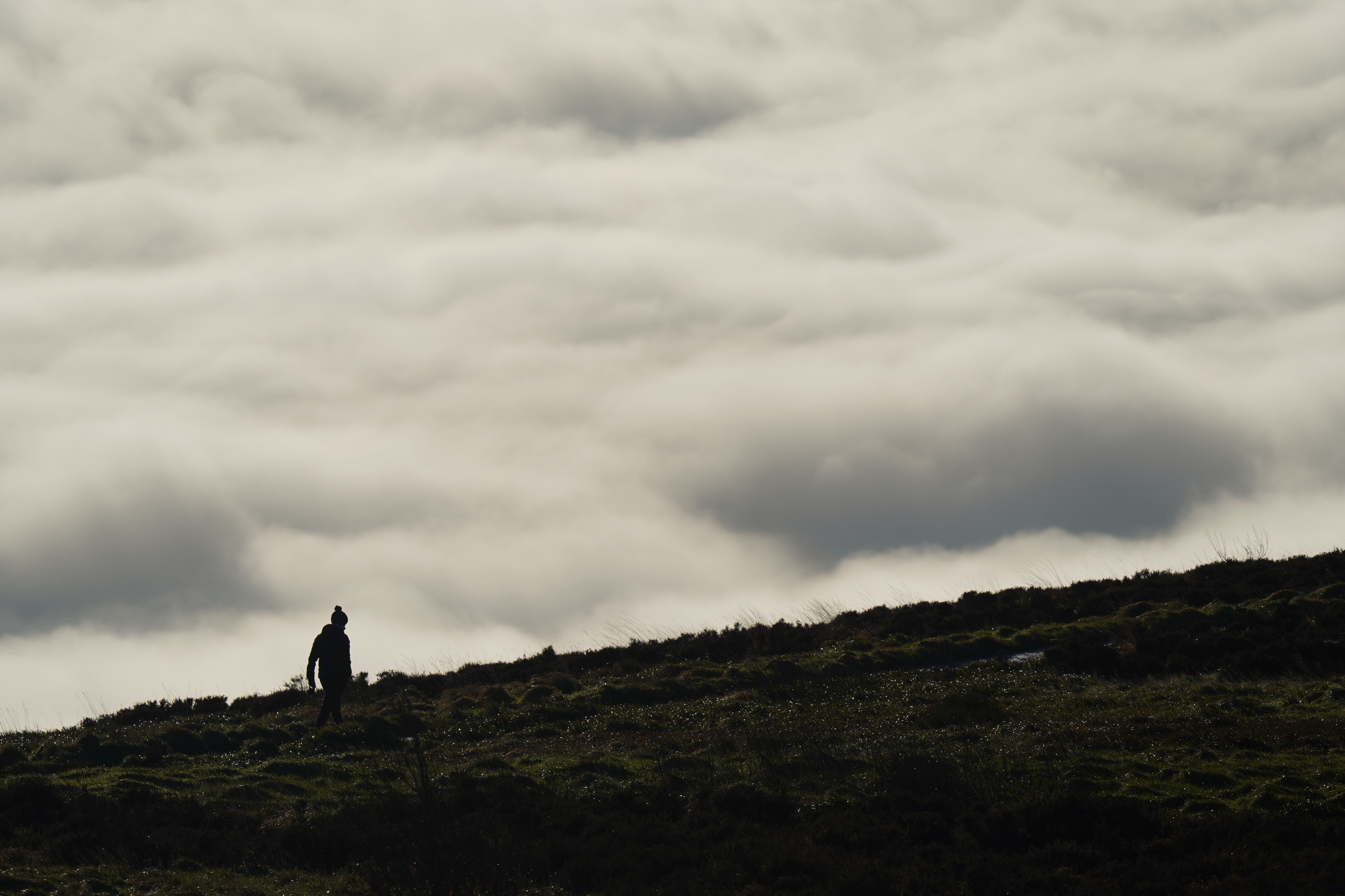 A lone hiker stands silhouetted on a hill, above a sea of clouds in Northern Ireland.