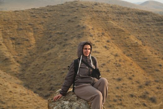 Woman in a hoodie sitting on a rock in a desert landscape during sunrise.