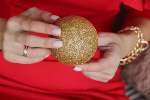 Hands holding a glittery gold ornament on a red background, festive and elegant.