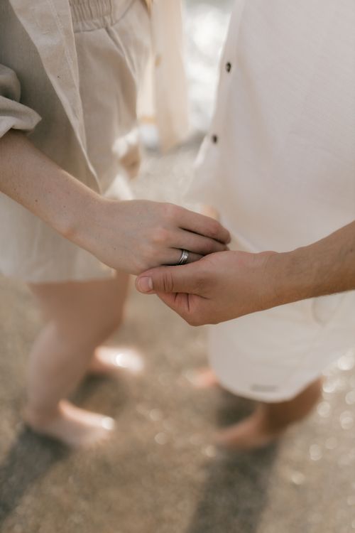 Free Close-up of a couple holding hands on a sunny beach, barefoot and in light attire. Stock Photo