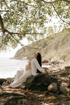 A serene beach scene with a pregnant woman relaxing under a tree, embracing nature.