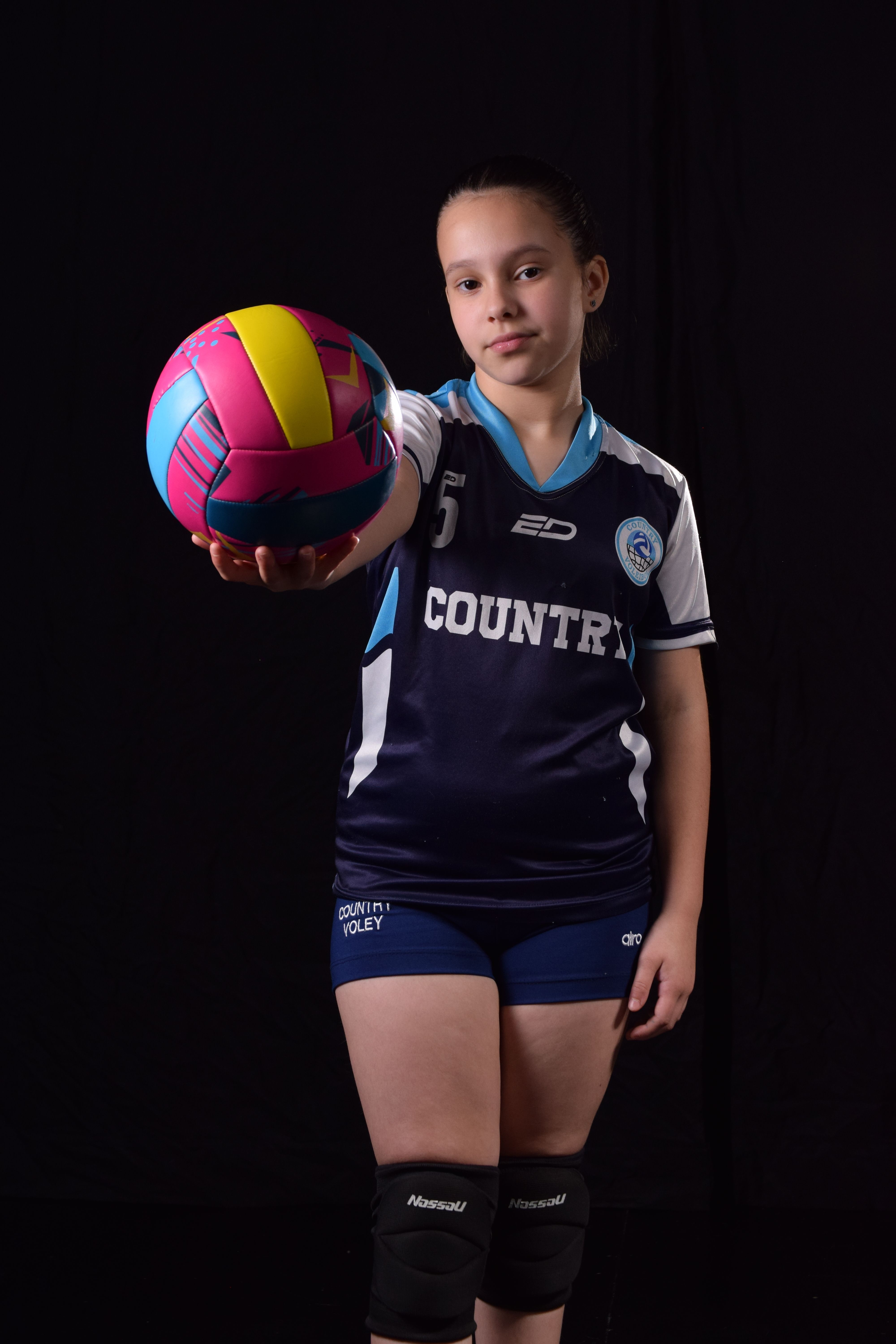 Portrait of a young female volleyball player holding a colorful ball indoors.