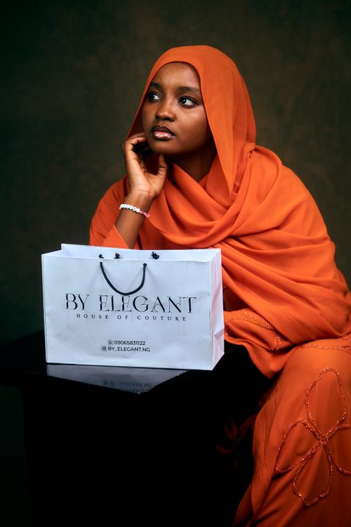 Free Woman in orange traditional attire posing with shopping bag against dark background. Stock Photo