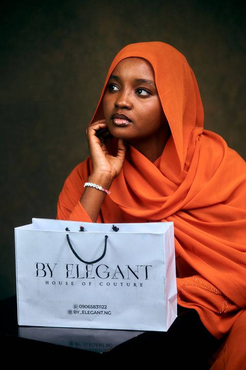Free Elegant young woman in orange hijab with a couture shopping bag indoors. Stock Photo