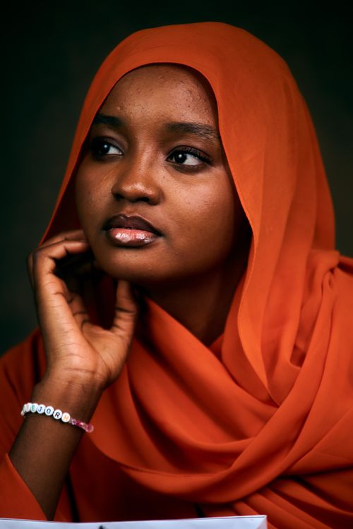 Free Beautiful portrait of an African woman wearing a bright orange hijab, deep in thought. Stock Photo