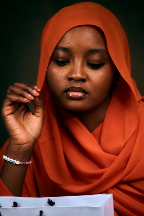 Free Thoughtful woman in an orange hijab looks down, with a bracelet visible on her wrist. Stock Photo