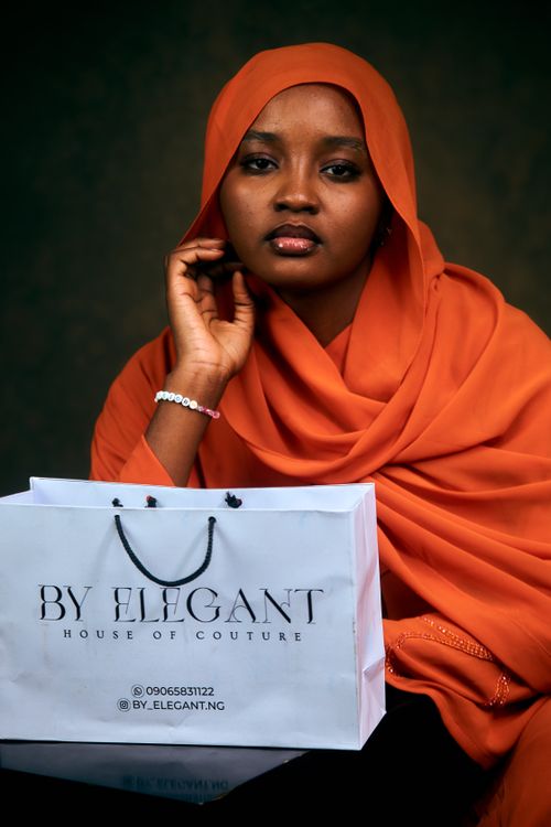 Free Young woman in an orange hijab sitting with a couture shopping bag. Stock Photo