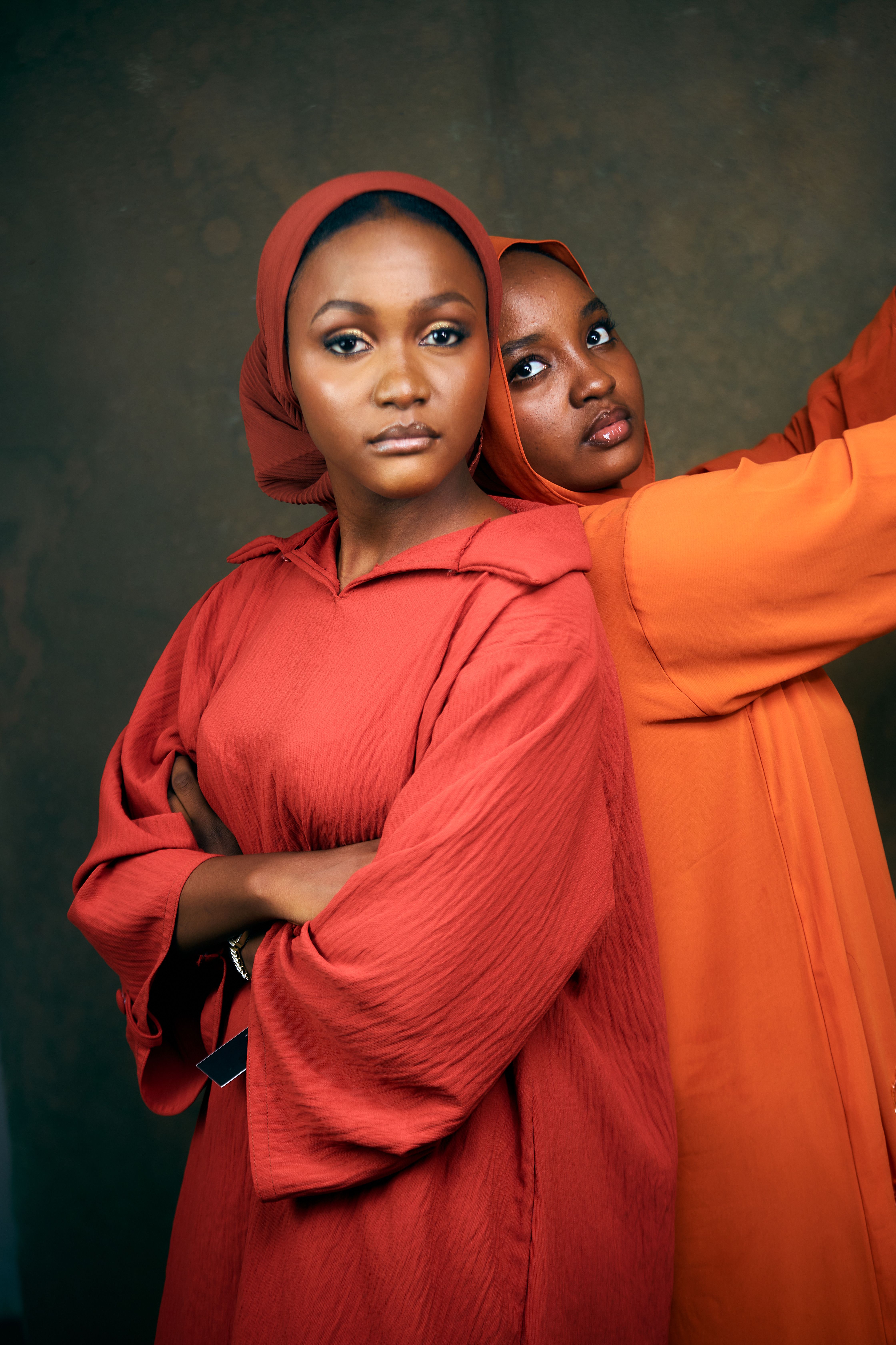 Two women in traditional attire pose confidently against a neutral backdrop.