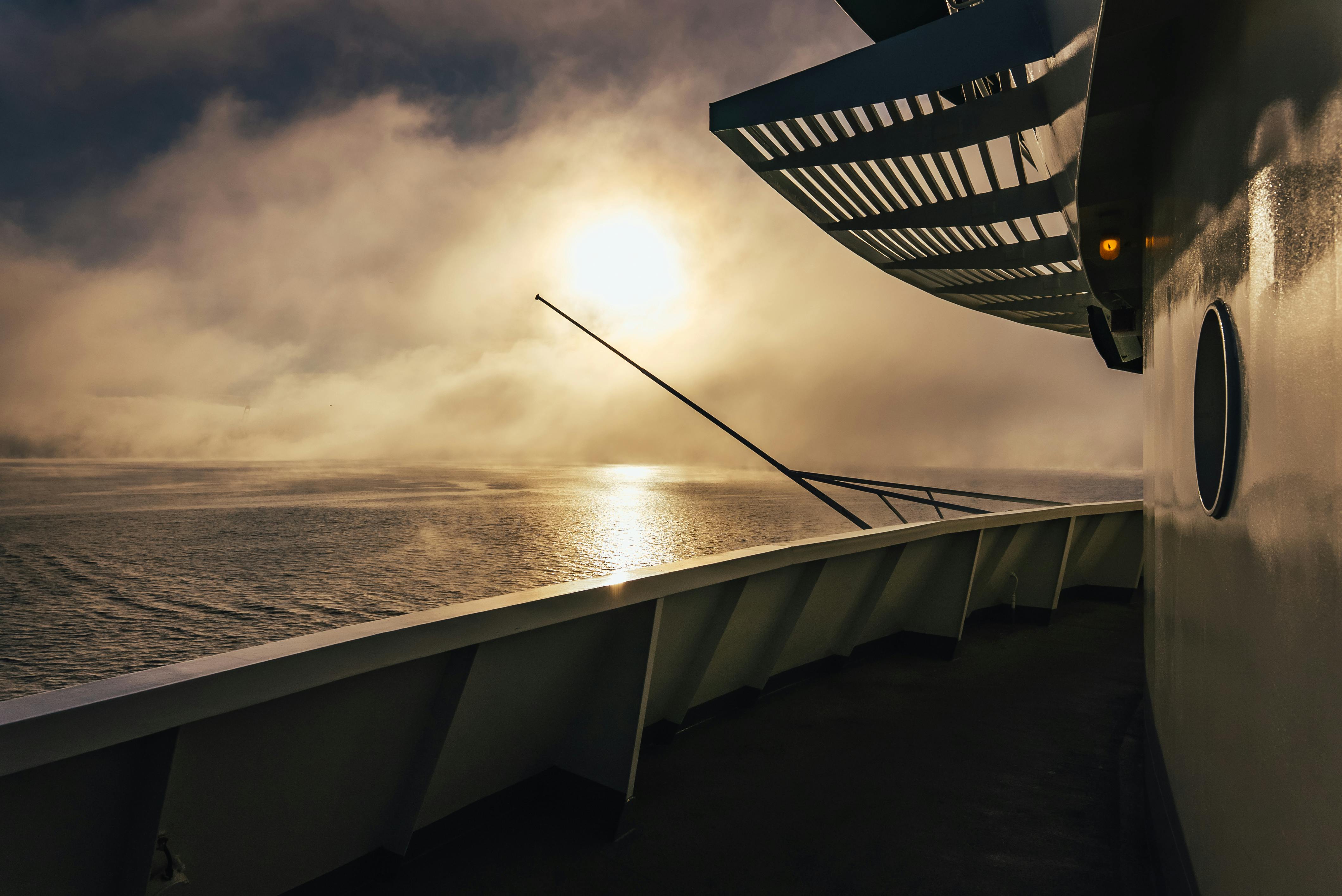 Ship deck overlooking the sea as sunlight breaks through low clouds and reflects on the water