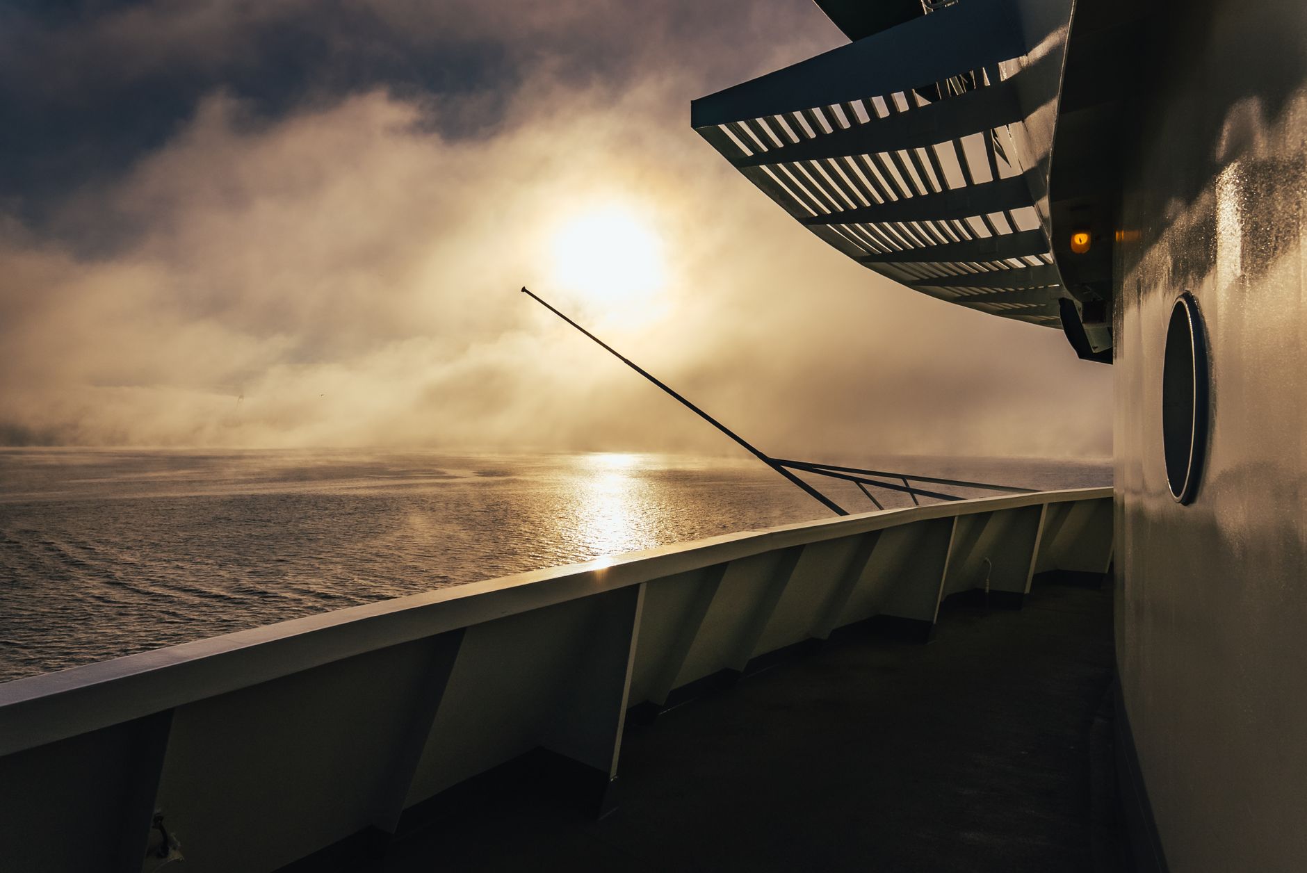 Atmospheric sunrise view from a Seattle ferry, enveloped in mist over calm waters, with the sun peeking through.