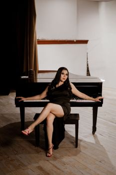 Sophisticated woman in a black dress sits gracefully at a grand piano, exuding elegance.