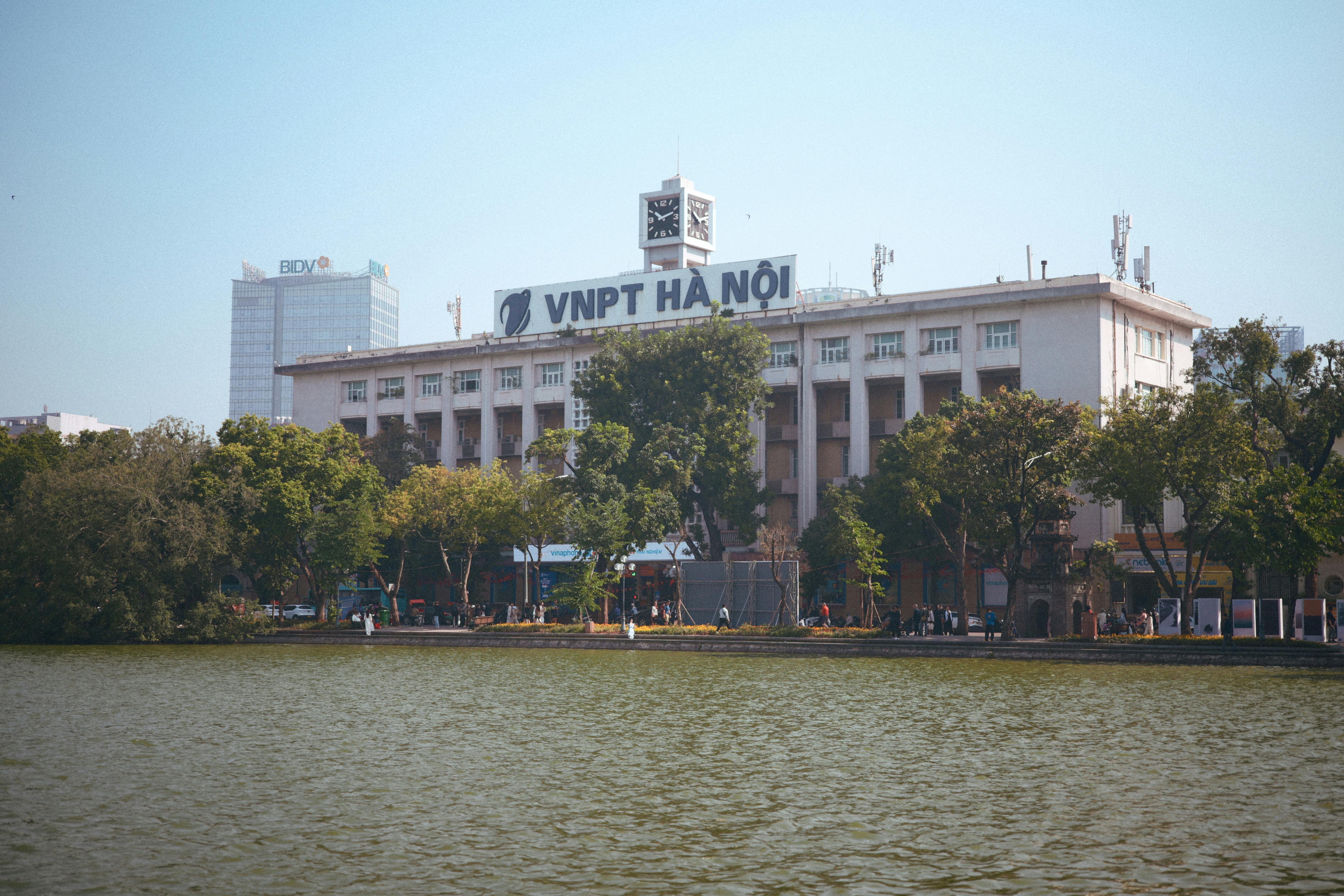 VNPT building in Hanoi by the lake with trees under a clear sky.