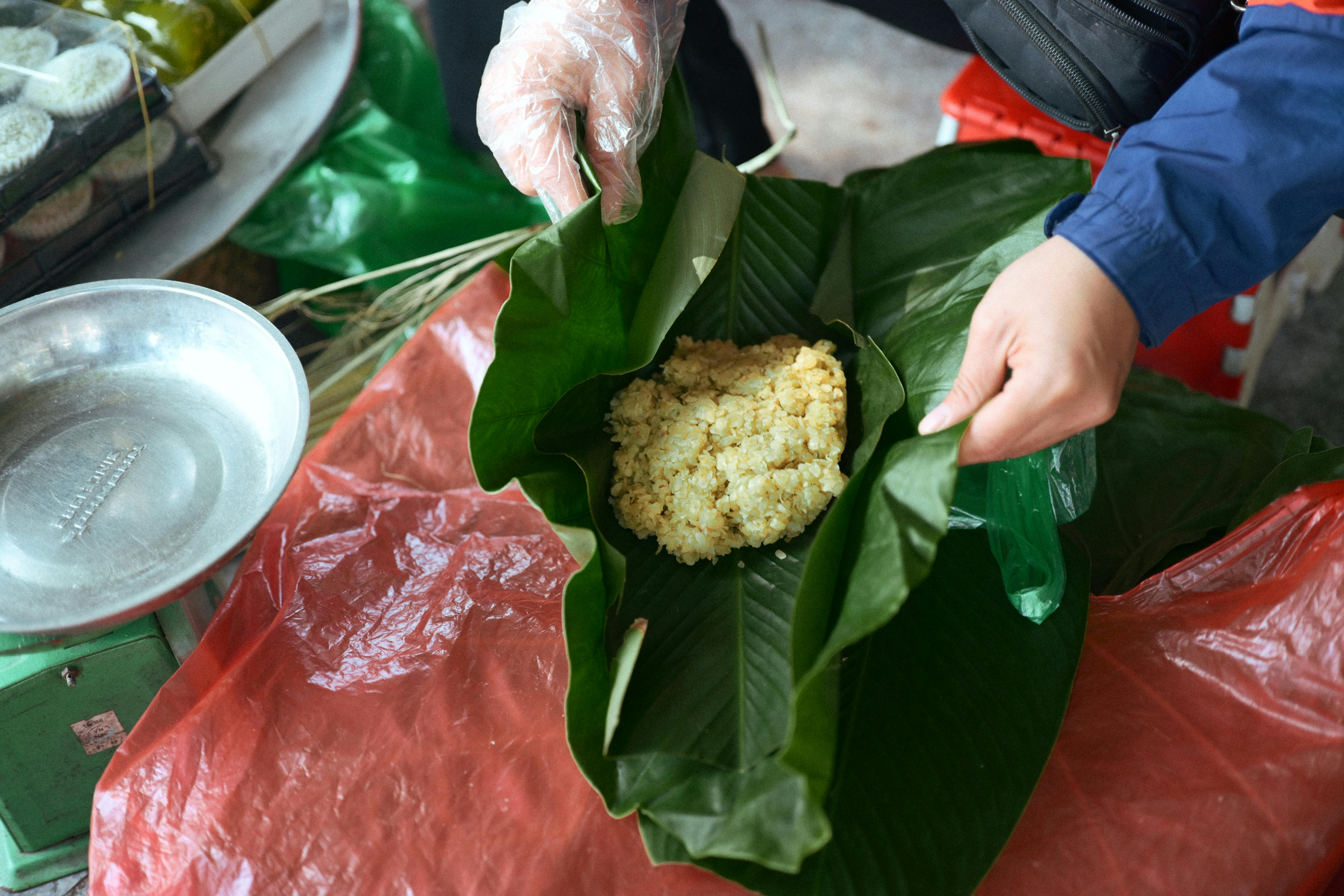 Street vendor preparing traditional dish wrapped in banana leaves with bare hands.