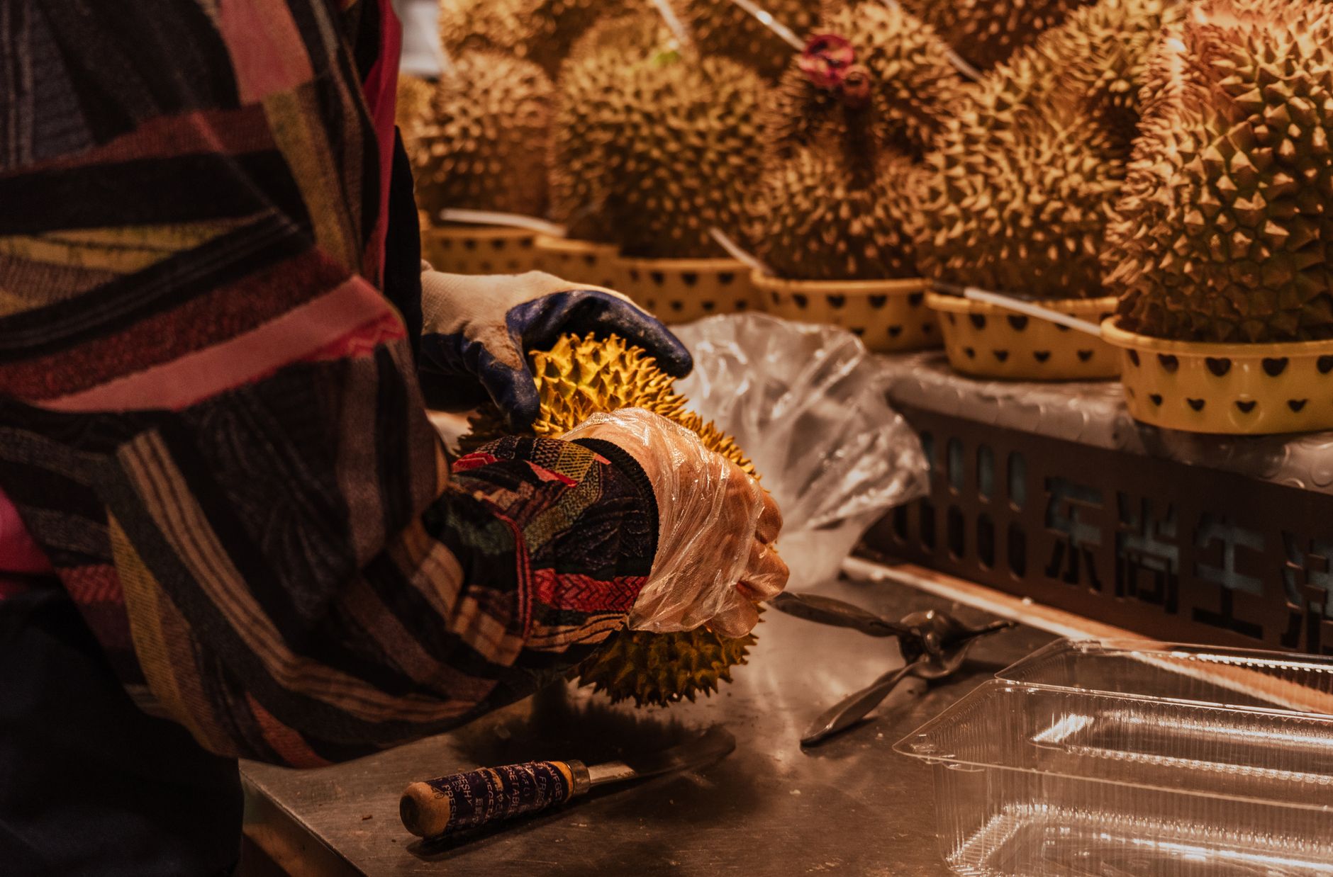 A person carefully handling a durian fruit in a market setting.