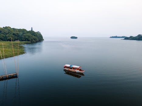 A serene aerial view of a boat on a tranquil lake surrounded by lush greenery under a clear sky.