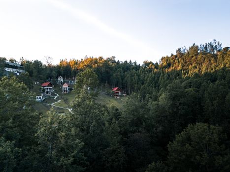 Scenic view of red-roofed cabins on a lush green hillside surrounded by dense forest.