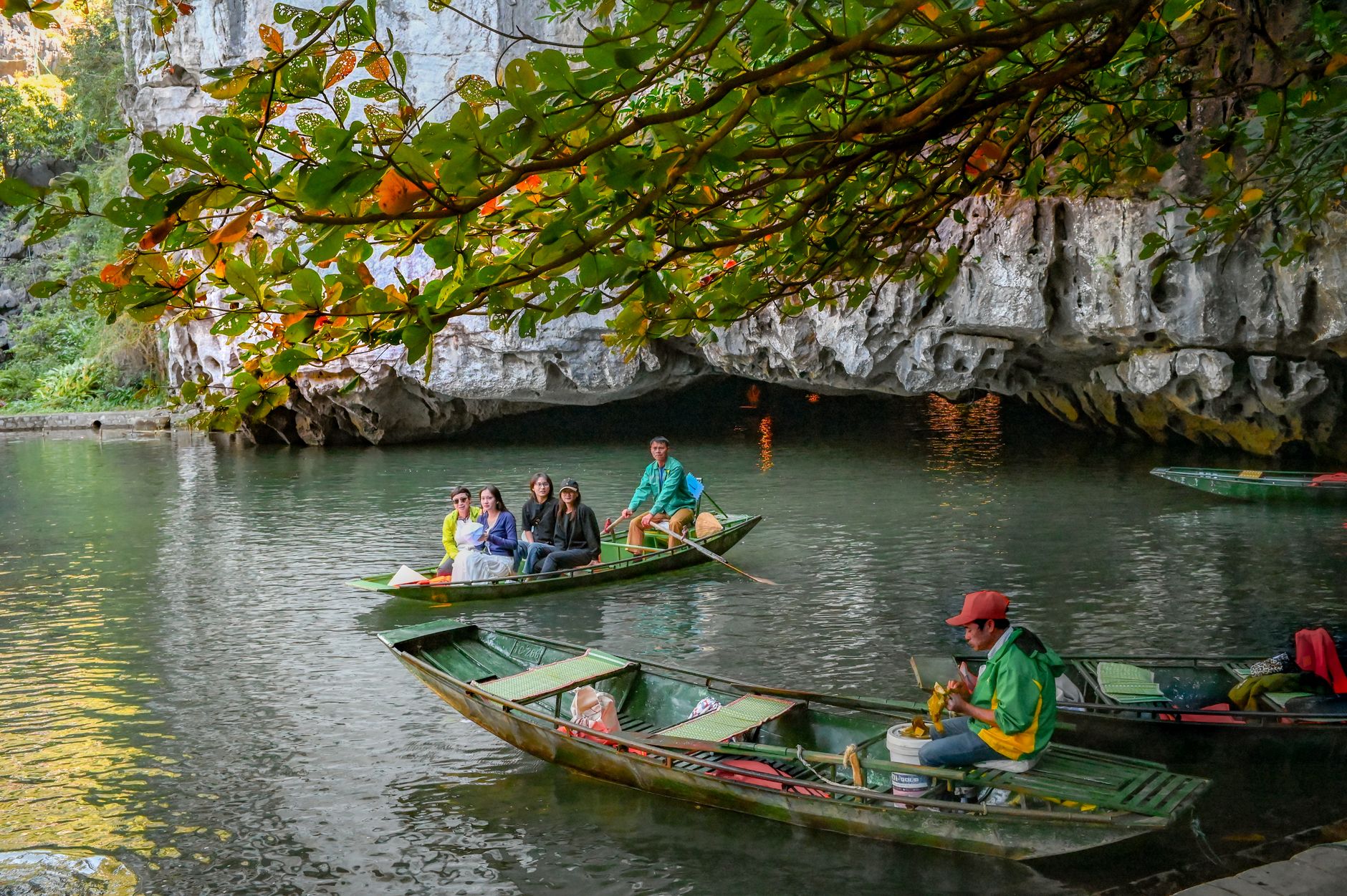 Tourists enjoy a scenic boat ride in Trang An Grottoes, Vietnam, surrounded by limestone caves and lush greenery.