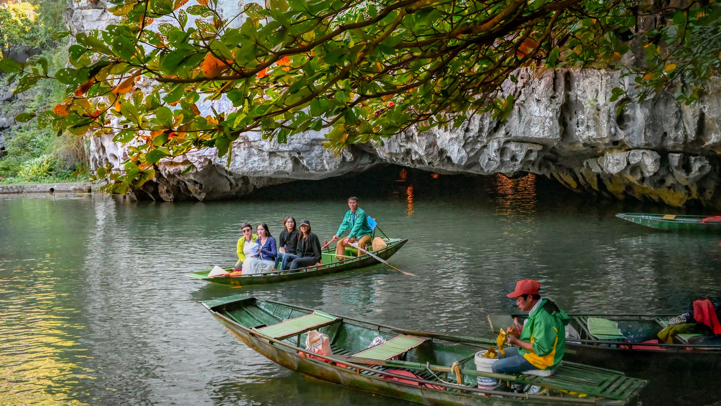 Tourists enjoy a scenic boat ride in Trang An Grottoes, Vietnam, surrounded by limestone caves and lush greenery.