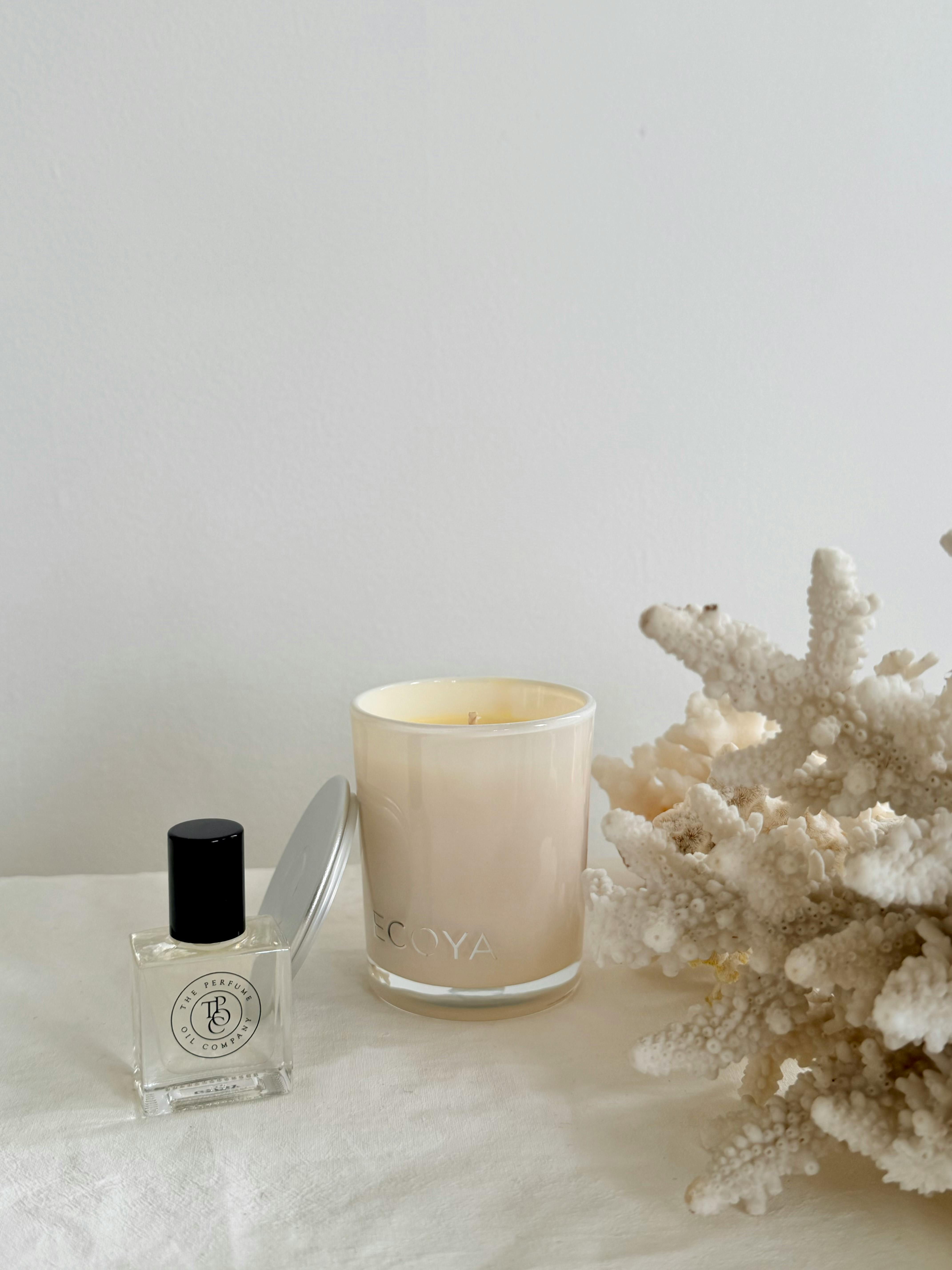 Elegant minimalist display featuring a candle, perfume, and coral accent.