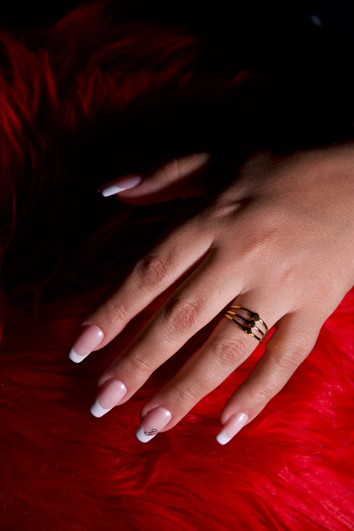 Close-up of a woman's hand with French manicure and golden ring on red background.