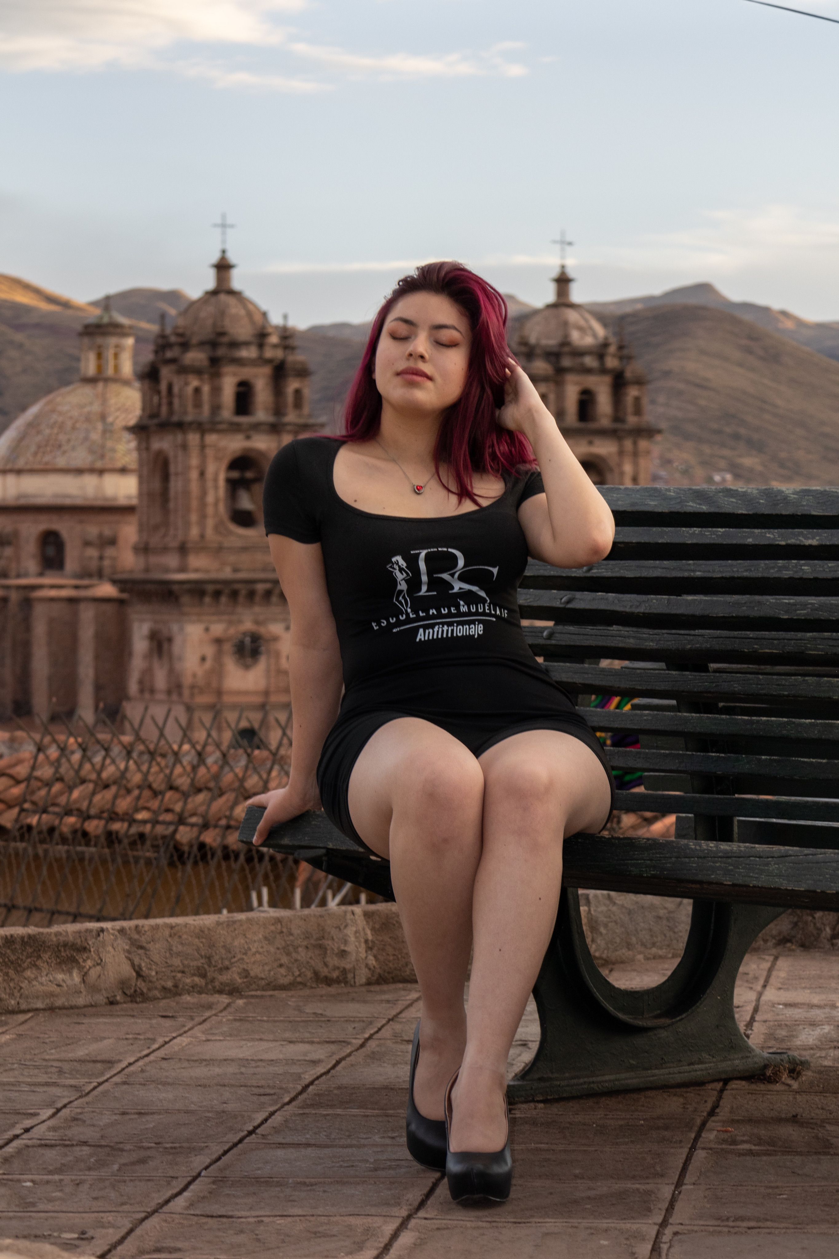 Woman sitting on a bench enjoying the view of colonial architecture under a blue sky.