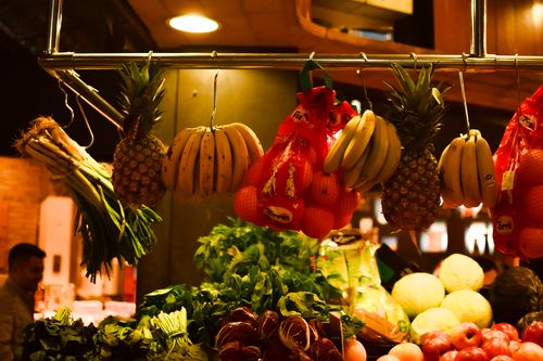 Free Colorful assortment of fresh fruits and vegetables hanging at an indoor market stall. Stock Photo