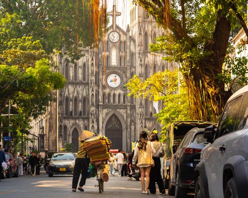 Free Vibrant street scene in Hanoi featuring St. Joseph's Cathedral surrounded by locals and vehicles. Stock Photo